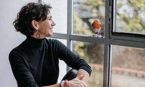 Claudia Potschigmann Business Coach für Frauen blickt aus einem Fenster zu einem Rotkehlchen