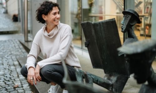Claudia Potschigmann Business Coach für Frauen sitzt vor einer Bibliothek und blickt auf eine Figur