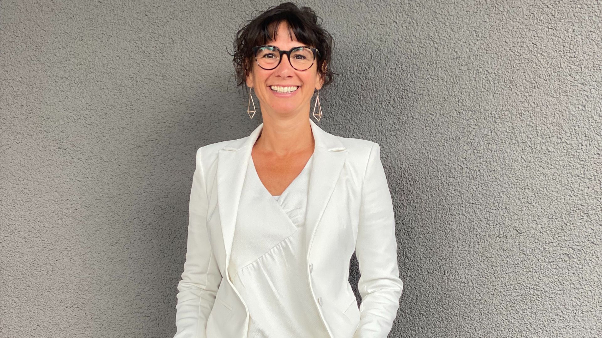 mages-business-coach-fuer-frauen-claudia-potschigmann-bei-ihrem-business-coaching-programm Claudia Potschigmann als Business Coach für Frauen lächelnd vor einer grauen Wand