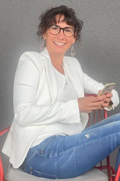 images-claudia-potschigmann-female-empowerment-coach-zur-kontaktaufnahme-2 Claudia, Female Empowerment- und Business-Coach, sitzt auf einem Stuhl mit einem iPhone in der Hand