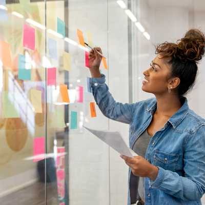 Eine Frau steht vor einer Glaswand und visualisiert mit Post Its Ideen zur Selbstfindung