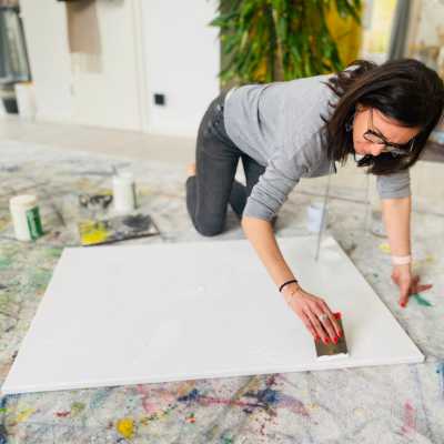 Claudia Potschigmann sitzt am Boden und spachtelt eine Leinwand bei einem Painting Workshop.