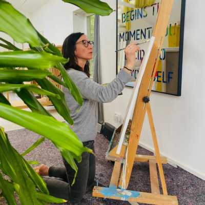 Claudia Potschigmann, Business- und Mental-Coach für selbständige Frauen, kniet am Boden, vor einer Leinwand und malt ein Bild.
