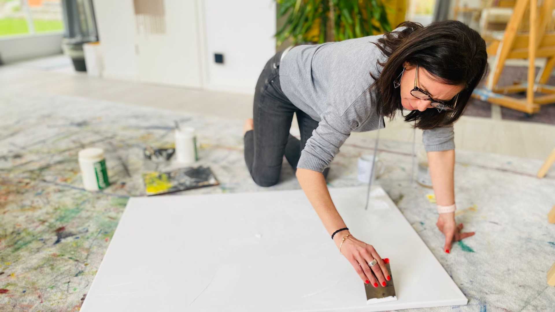 Claudia Potschigmann kniet am Boden, mit einer Leinwand, bei einem Malworkshop